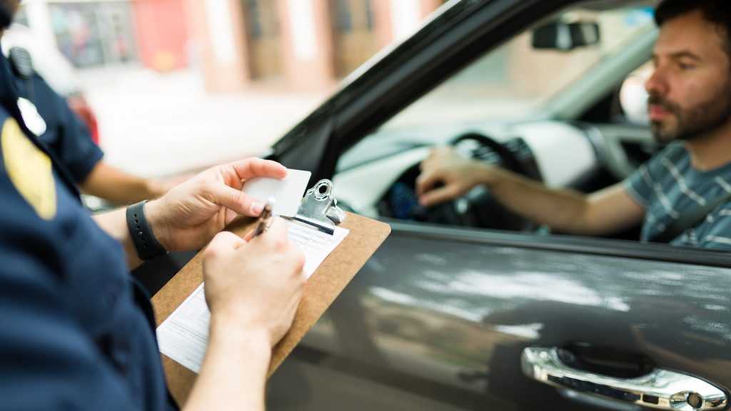 Stock photo of a police officer writing a traffic ticket to a driver